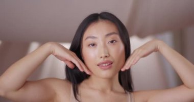 Güzel Asyalı kadın temiz cilt yoluyla mutlu hissediyor. Güzellik kızı hareketi ve kameraya poz vermek. Yumuşak bir yüze ve sağlıklı bir vücuda dokunmak. Yaklaş, gülümse. Genç ve güzel ten kavramı.