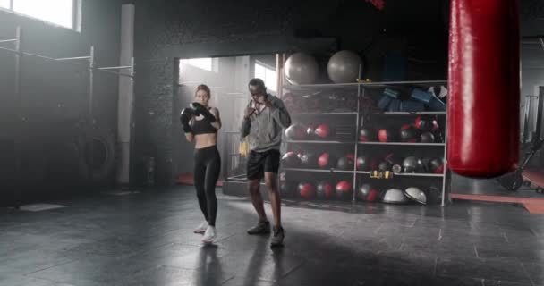 迷人的女人穿着运动服和拳击手套在拳击馆和非洲裔美国人私人教练一起训练 适合一起进行高强度锻炼的人 混合种族体育概念 — 图库视频影像