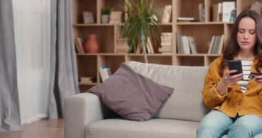 Çekici beyaz kadın kredi kartı tutuyor ve ödeme için mobil uygulama kullanıyor. Arka planda kitaplıklarla online alışveriş yapan ciddi bir kadın. Müşteri, alıcı, müşteri kavramı.