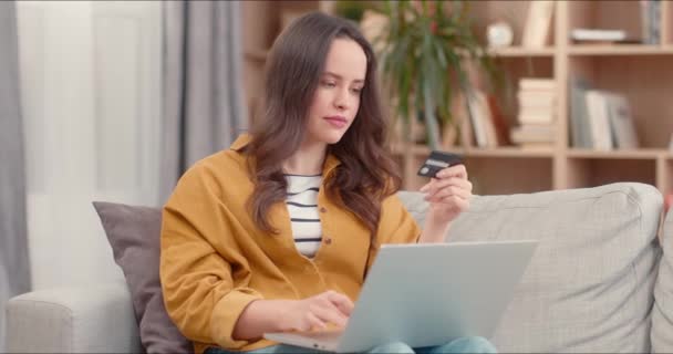 迷人的高加索女人在家里的图书馆网上购物 年轻而暴躁的女人拿着信用卡 使用笔记本电脑 用数字设备购买容易 积极的女士对购物感到快乐 — 图库视频影像