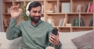 Yakışıklı genç adam ev kütüphanesinde eğleniyor. Kulaklıklı, cep telefonlu, video izleyen ve en sevdiği müziği dinleyen çekici bir erkek. Aktif olarak elinizi şarkıda sallayın.