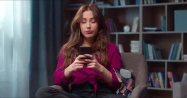 Çekici beyaz kadın, rahat oturma odasında koltukta oturuyor. Telefon kullanan çekici bir kadın, çevrimiçi alışveriş sitelerine kayıyor ve büyük indirime şaşırıyor. Dijital teknoloji kavramı.