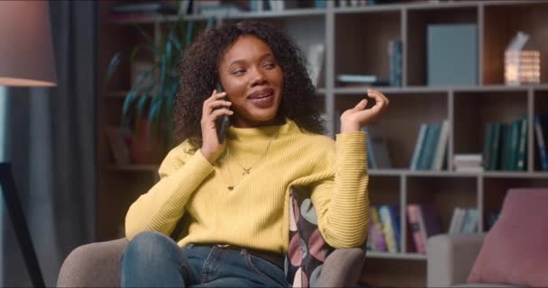 快乐的非洲裔美国女人在她的手机和放松在图书馆 年轻女性积极地谈论并高兴地同意即将与伴侣见面的日期 — 图库视频影像