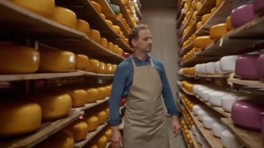 Çekici beyaz işçi fabrikanın ürettiği peynir tekerleklerini takdir ediyor. Depoda yürüyen ve üretim oranından memnun olan memnun bir adam. Süt ürünleri ahşap raflarda yatıyor..