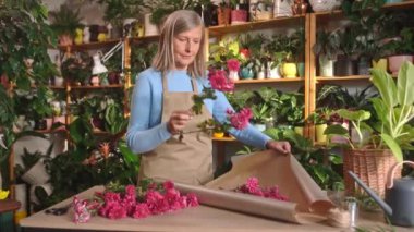 Çekici beyaz kadın çiçekçi güzel bir buket kırmızı çiçek yapıyor. Müşteri için harika bir kompozisyon hazırlıyorum. Çiçekçide çalışıyorum. Dekorasyon. Düzenleme konsepti.