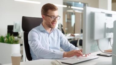 Ofiste bankacılık ticaretiyle uğraşan Kafkasyalı bir yöneticiye zum yapıyorum. Mutlu adam şef için bilgisayar, mesaj ya da tamamlama kullanıyor. Gülümsüyor ve kameraya bakıyor..