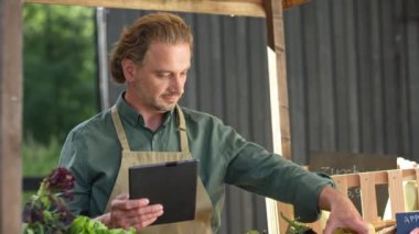 Çiftlik pazarında çalışırken tablet bilgisayar kullanan çalışkan bir beyaz satıcı. Etrafta doğal sebze ve meyve dolu sandıklarla meşgul bir adam var. Üretimin tamamlanması müşteri sırasına göre sayılıyor.