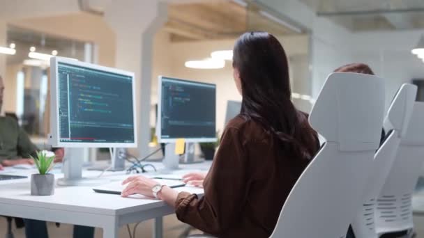 刻苦工作的女程序员在计算机工作时与伴侣交谈的侧视图 屏幕上可见的程序代码 年轻人在办公室里交流 开发人员概念 — 图库视频影像
