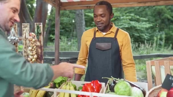 有吸引力的白人男性购物者在当地市场上选择或购买天然蔬菜 勤劳的多族裔工人销售有机食品 持有终端用信用卡付款 — 图库视频影像