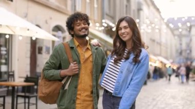 Mutlu gülümseyen genç bir çift kafeteryalarla süslü bir caddede duruyor ve keyifli bir şekilde kameraya bakıyor. Neşeli yakışıklı koca şehirde güzel bir eşi kucaklıyor. Aile, aşk konsepti