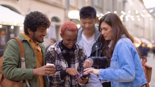 画面を見て話す携帯電話を使用してコーヒーと街の中心部に立って陽気な多民族の若い友人の観光客の肖像画を閉じます 幸せな男性と女性がスマートフォンでタップ — ストック動画