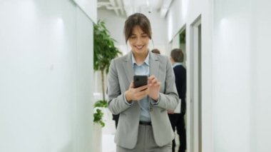 Beyaz koridorda iş arkadaşlarının durduğu beyaz koridorda yürüyen güzel bir beyaz kadın yönetici. Akıllı telefon kullanan ve mesajlaşan genç bir kadın. Neşeli bir gülümseme. İyi hislerim var..