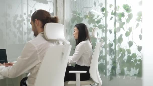 由两名身穿白衬衫和在现代办公室工作的混血工人组成的小组 当男人忙着用笔记本电脑时 亚洲女人在镜头前开心地笑着 公司治理 协作概念 — 图库视频影像
