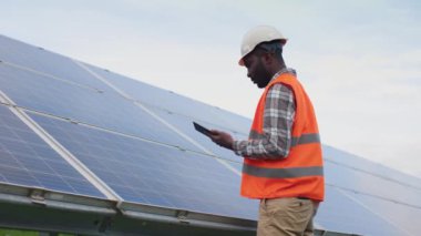 Alternatif enerji kaynakları üretiminde çalışan Afrikalı Amerikalı mühendisin portresi. Miğferli ve koruyucu yelekli endüstri çalışanı sayısal tablet tutuyor ve görevler yapıyor..