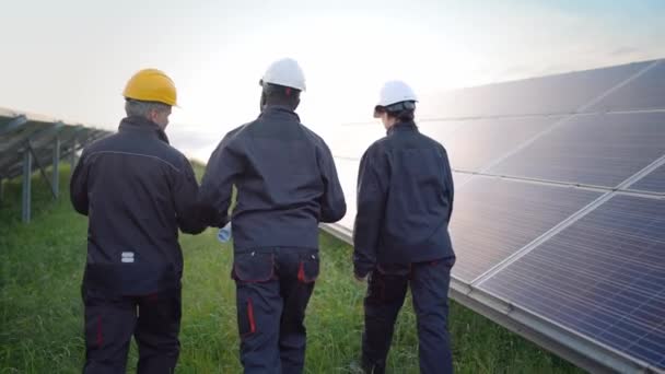 生态工程师背向行走的肖像 光伏太阳能电池板 穿着防护服 头戴安全帽的员工讨论创新绿色能源 — 图库视频影像