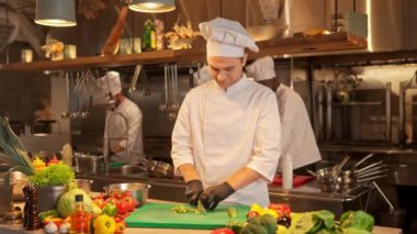 Üniformalı bir aşçının portresi salatayı hazırlamak için yeşil salatalığı öğütüyor ya da mutfak bıçağıyla güveç yapıyor. Şef profesyonel restoran mutfağında lezzetli yemekler pişiriyor..