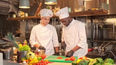 İki çok kültürlü aşçı, iş yerinde, profesyonel restoran mutfağının arka planında iletişim kuruyor. Baş aşçı yemek tariflerini açıklıyor. Afro-Amerikalı erkekler taze kırmızı biber öğütüyor..