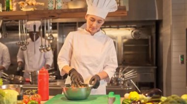 Profesyonel restoran mutfağında vejetaryen salatası hazırlayan kadın şefin portresi. Özel üniforma ve eldiven giymiş bir kadın marul yaprakları ve sebzeleri derin bir sakso ile karıştırır..