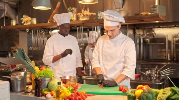 アフリカ系アメリカ人シェフはおいしいベジタリアン料理の調理法を教えています 多文化料理人の専門のキッチンでの作業プロセス キッチナー細切り新鮮な赤唐辛子 — ストック動画