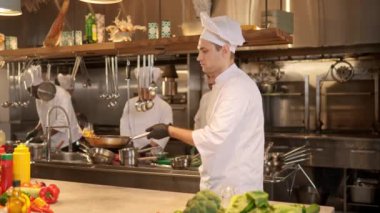 Profesyonel usta şefin portresi tavada et parçaları kızartıyor. Özel bir üniforma giymiş yetişkin aşçı. Lokanta mutfağında reçeteyle lezzetli yemekler hazırlıyor..
