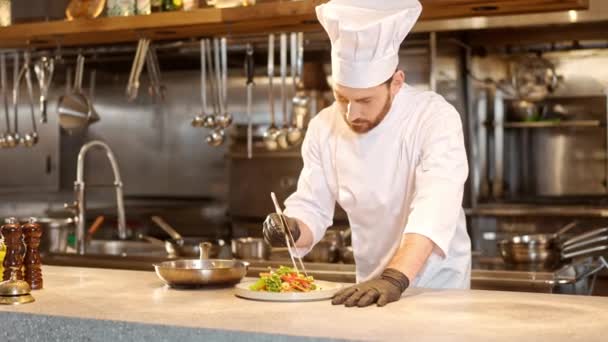 专业的大胡子厨师制作蔬菜沙拉 并将菜放在白盘上 现代餐厅厨房里穿着特殊制服烹调食物的男厨师 — 图库视频影像
