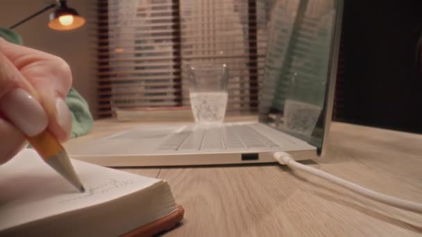 クローズアップ撮影 カメラはゆっくりとテーブル表面の物体に向かって移動します 人の手は鉛筆でノートを作成し 机の上のコンピュータで作業し ラップトップを入力します オンライン学習の概念 — ストック動画