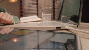 Yakın plan çekim. Kamera masa yüzeyindeki nesnelere doğru yavaşça hareket ediyor. Elle kayan akıllı telefon ekranı, masadaki dizüstü bilgisayarda çalışan ve gaz köpüklü su içen insanlar..