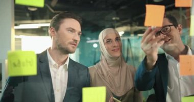 Çok ırklı bir grup insan üzerinde çıkartmalar ve çizimler olan cam bir tahta düşünüyor. Şirketin ekonomik durumunu analiz eden zeki işçiler. Analitik iş. Takım çalışması kavramı.