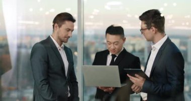 Takım elbiseli iyi görünümlü yöneticiler cam ofiste iletişim kuruyor. Çekici ortaklar kolektif takım çalışmasını tartışıyor. Sohbet sırasında dizüstü bilgisayar kullanmak. İletişim kavramı.