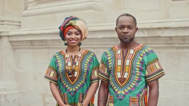 穿着格式化衣服的非洲夫妇 身着传统节日服装的男男女女都在看着摄像机 在头巾里 多种族男人拥抱女人 快乐的非洲夫妻笑着 — 图库视频影像