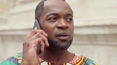 Afrikalı erkek portresi. Süslü kıyafetler giymiş çok kültürlü bir adam. Çok ırklı sakallı bir adamın telefonu. Üçlü giyinmiş Afrikalı adam telefonla konuşuyor..