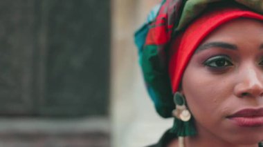 Afrikalı kadın portresinin yarısını kapat. Makyajlı ve türbanlı çok kültürlü bir kadın. Aydınlık mücevherler içindeki çok ırklı bir kadının detaylı görüntüsü. Geleneksel türban takmış ciddi bir kadın..