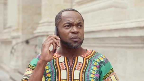 非洲男人在电话中交谈的肖像 男性穿着传统装饰服装的特写 穿着非洲服装的中年男子 男人用手势表达出来 并在电话里辩论 — 图库视频影像