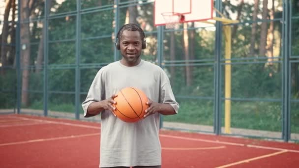 Kulaklıklı Afro Amerikalı Bir Adam Basketbol Sahasında Duruyor Gülümseyerek Kameraya — Stok video