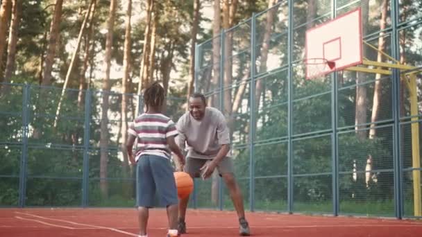 非裔美国人的父亲和儿子打篮球 扔球圈与太阳耀斑 孩子和爸爸在公园和打篮球玩得很开心 男人和男孩跳起来 把球扔到篮筐里 — 图库视频影像