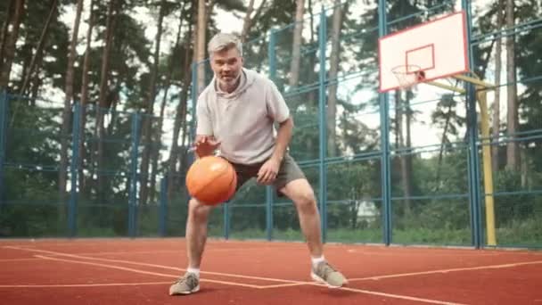 Взрослый Мужчина Играет Мячом Баскетбольной Площадке Мужчина Смотрит Камеру Улыбкой — стоковое видео