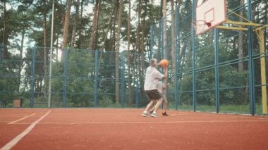 Küçük şirin çocuk dışarıda, dışarıda basketbol oynarken zıplıyor. Neşeli çocuk babasıyla basketbol oynuyor. Erkek aile üyeleri birlikte vakit geçiriyor..