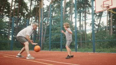 Baba ve oğul oyun alanında birlikte basketbol oynuyorlar. Basketbol sahasının arka planında topu yakalamaya çalışan tatlı çocuk. Dışarıda vakit geçirmek. Aktif spor oyunları oynamak ve eğlenmek..