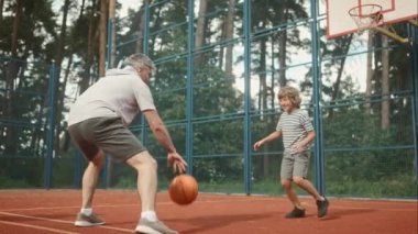 Sahada basketbol oynayan, top süren, top süren, salyalarını akıtan, küçük oyuncuyu eğiten yetişkin bir adam ve genç çocuğun vücut boyu portresi. Açık havada zaman geçirme kavramı