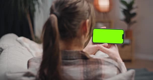坐在沙发上看绿色屏幕的女人 女性坐在沙发上 看着彩色的按键屏幕 拿着智能手机看系列片的女人客厅里的女士在做小玩艺儿 — 图库视频影像