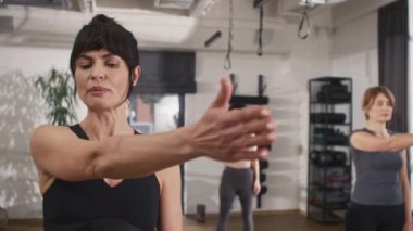 Güzel bayan koç müşterilerine spor salonundaki egzersizleri izah ediyor ve gösteriyor. Çalışkan kadınlar antrenörlerinin hareketlerini takip ederler. Egzersiz konsepti.