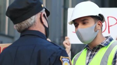 Polis isyanı bastırmaya çalışıyor. Koruyucu maske ve miğfer takan genç adam, protestocu insan hakları gösterisinde polislere bağırıyor ve bağırıyordu. Karantina karşıtı protesto.