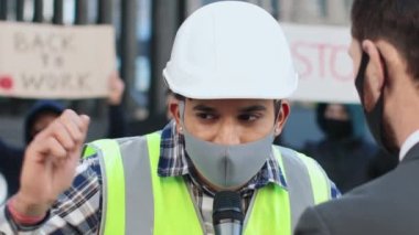 Koruyucu maskeli işçiler haber kanalına röportaj veriyor. Gazeteciler aşı karşıtı protestolara katılan kişileri sorguluyor. Halk gösterilerinde pankart ve posterleri olan insanlar..