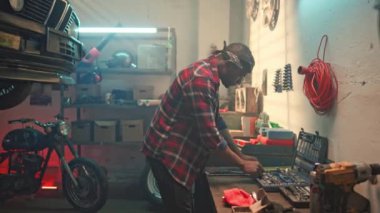 Kollarını kavuşturup garajda kameraya bakan yakışıklı bir erkek portresi. Afro-Amerikan bir adam, oto tamircisi, araba atölyesinde işini bitiriyor ve her ihtimale karşı gerekli aletleri koyuyor..