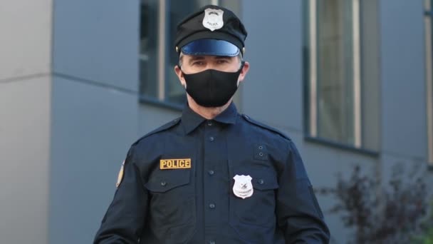 戴着医疗面罩的警官看着摄像头 戴着防护面具的英俊美国警察的户外肖像 看上去严肃而自信地呆在街上 警察肖像 执勤警察 — 图库视频影像