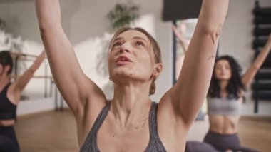 Müşterileriyle yoga egzersizi yapan beyaz tenli güzel bir kadın eğitmenin portresi. Spor paspaslarında oturan ve eğitim hocalarıyla egzersizleri tekrarlayan kadınlar. Sağlıkla ilgilenmek.