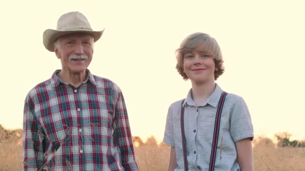 水平ショット 陽気な老人と少年がライに立っている 幸せな祖父と孫が畑に立っている チェッカーされたシャツとストロー帽子の男性農家 農業か耕作か — ストック動画
