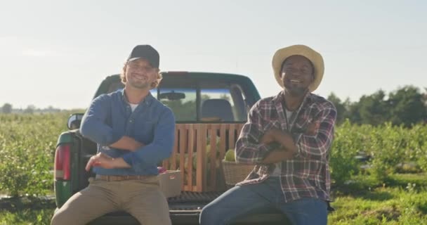 ピックアップトランクに座っている2人の多文化農家 農業従事者の幸せな農業従事者が栽培シーズンを終えました 2人の男が腕を横切ってカメラで微笑んだ 夏の収穫シーズン — ストック動画