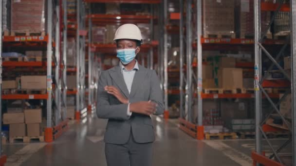 非洲裔美国妇女在仓库里乱跑 身穿灰色西服 戴着防护服 戴着安全面具的女性 公司经理 背对着架子 两臂交叉 族裔多样性 — 图库视频影像
