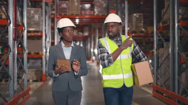 2人のアフリカ系アメリカ人産業労働者が倉庫を歩いている タブレットを持ち メモを作る女性マネージャー コントラクターのジェスチャーとスーパーバイザーコンサルタントと話す — ストック動画